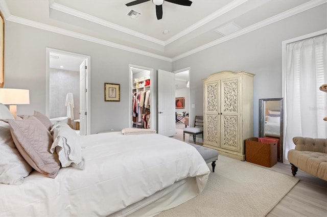 bedroom featuring light wood-type flooring, crown molding, ceiling fan, a tray ceiling, and a spacious closet