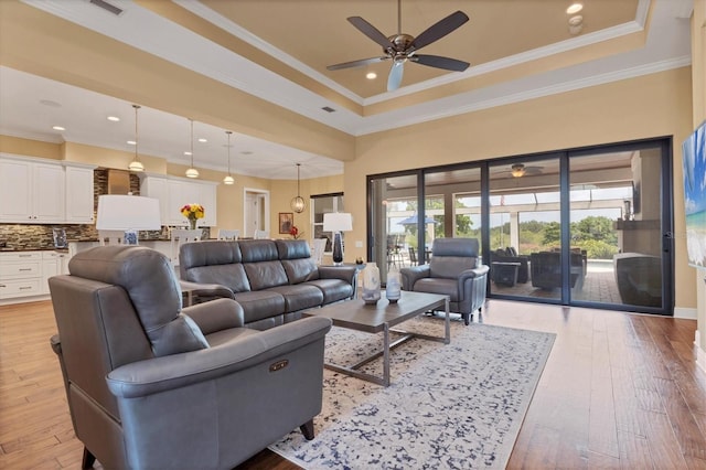 living room featuring ceiling fan, a raised ceiling, a healthy amount of sunlight, and light hardwood / wood-style floors