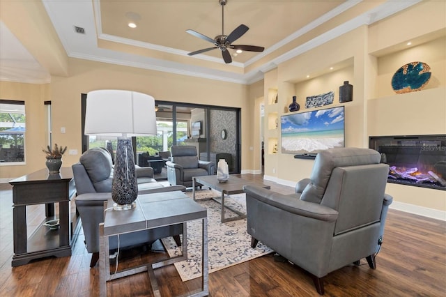 living room featuring ceiling fan, dark hardwood / wood-style flooring, a raised ceiling, and ornamental molding