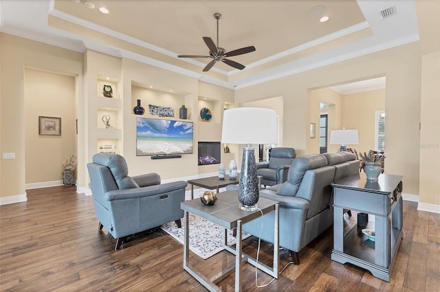 living room featuring ceiling fan, dark hardwood / wood-style flooring, a tray ceiling, and ornamental molding