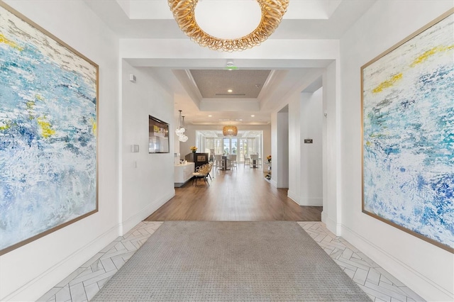 hallway featuring a notable chandelier, light wood-type flooring, and a raised ceiling