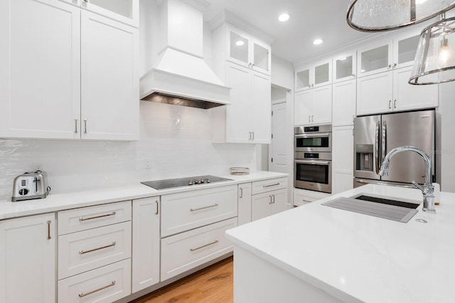 kitchen featuring stainless steel appliances, hanging light fixtures, premium range hood, backsplash, and light wood-type flooring