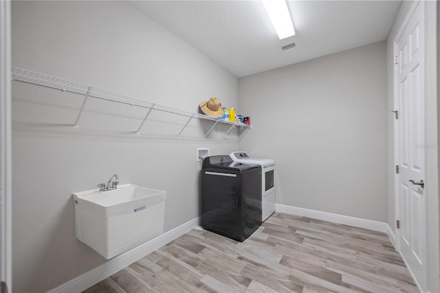 clothes washing area with washer and dryer, a textured ceiling, and light wood-type flooring