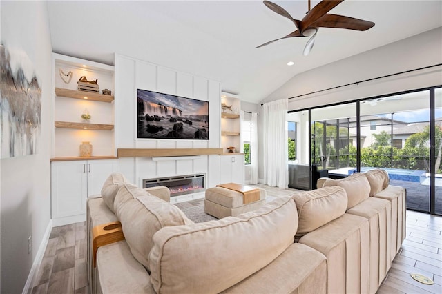 living room featuring light hardwood / wood-style flooring, vaulted ceiling, a large fireplace, ceiling fan, and built in features