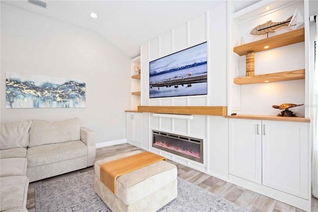 living room featuring light hardwood / wood-style floors, vaulted ceiling, and built in features