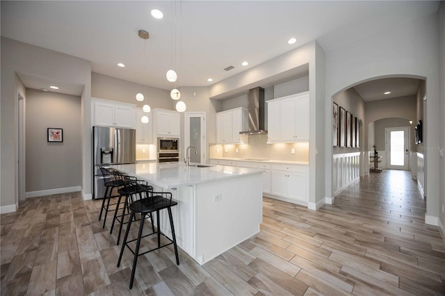 kitchen with a spacious island, wall chimney exhaust hood, stainless steel appliances, and white cabinets