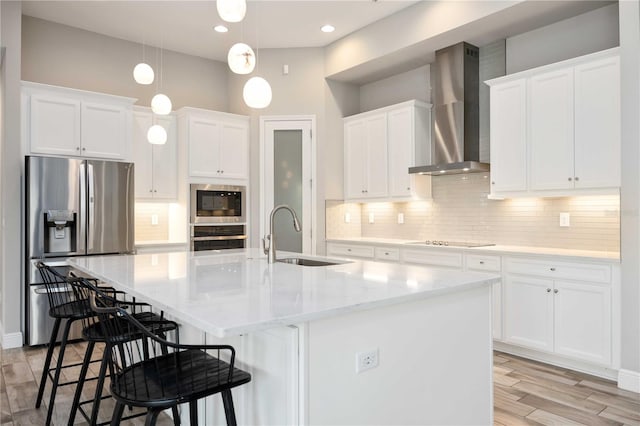 kitchen featuring a center island with sink, stainless steel appliances, sink, white cabinets, and wall chimney exhaust hood