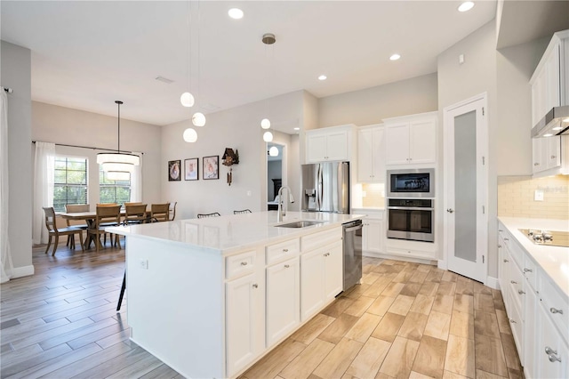 kitchen featuring stainless steel appliances, white cabinets, decorative light fixtures, sink, and a kitchen island with sink