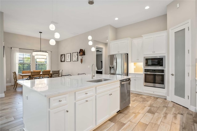 kitchen with a center island with sink, sink, white cabinetry, stainless steel appliances, and hanging light fixtures