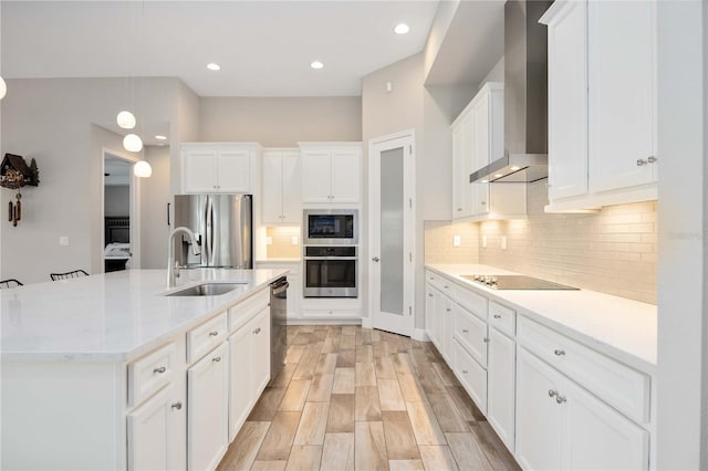 kitchen with a center island with sink, stainless steel appliances, white cabinets, wall chimney range hood, and sink