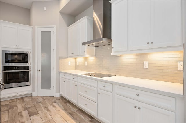 kitchen featuring decorative backsplash, black appliances, white cabinets, and wall chimney exhaust hood