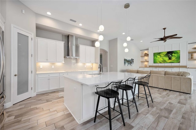 kitchen featuring a center island with sink, white cabinets, wall chimney range hood, a breakfast bar, and sink