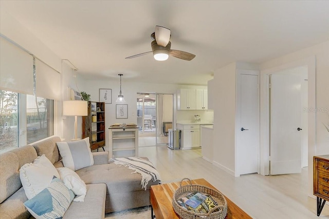 living area with baseboards, light wood-style flooring, and a ceiling fan