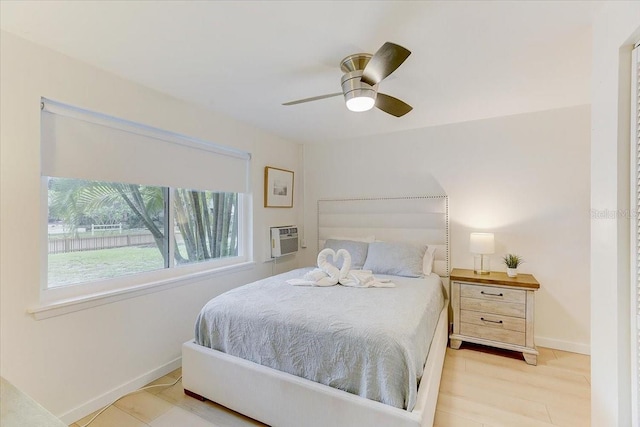 bedroom featuring baseboards, wood finished floors, a wall mounted air conditioner, and a ceiling fan