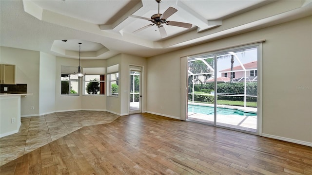 unfurnished living room with coffered ceiling, light hardwood / wood-style floors, a raised ceiling, and ceiling fan