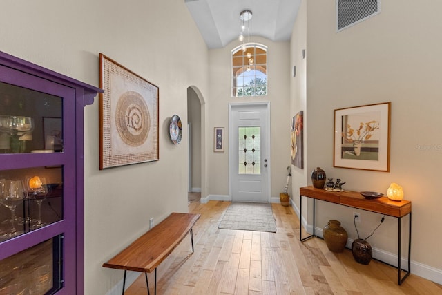 foyer featuring arched walkways, visible vents, light wood-style flooring, high vaulted ceiling, and baseboards