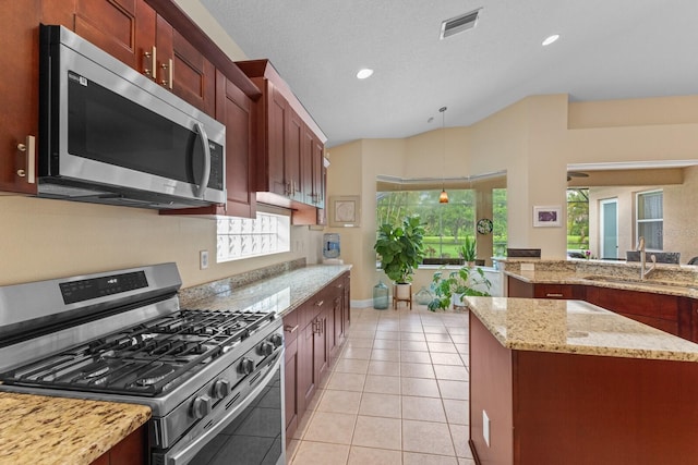 kitchen with appliances with stainless steel finishes, light tile patterned flooring, a sink, light stone countertops, and plenty of natural light