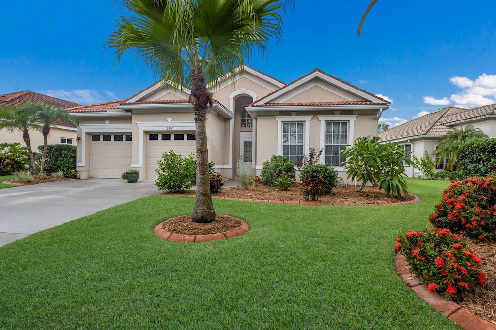 6690 Tailfeather Way, Bradenton, FL 34203 - mediterranean / spanish house featuring driveway, an attached garage, a front lawn, and stucco siding