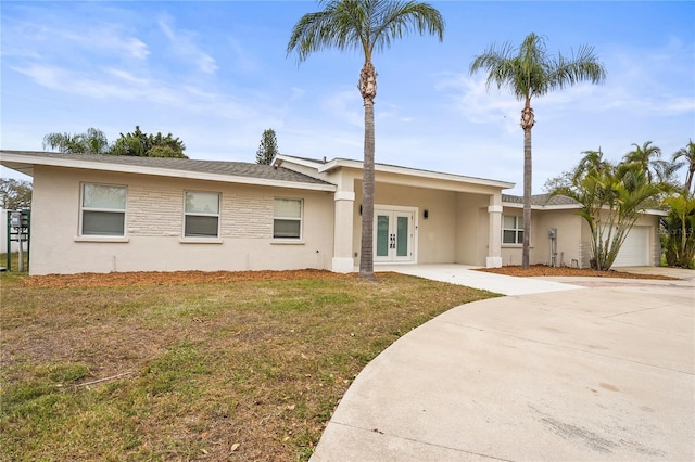 view of front of home with a front lawn, stucco siding, driveway, french doors, and a garage