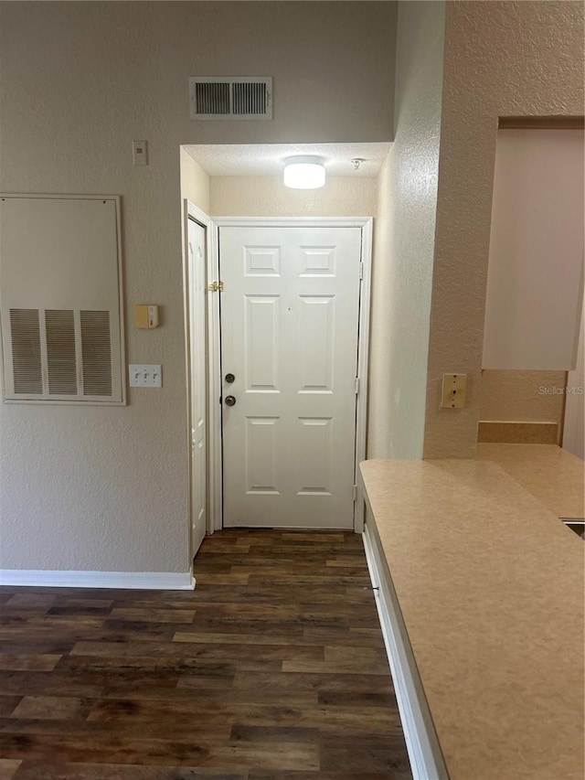 hallway featuring a textured wall, dark wood-type flooring, visible vents, and baseboards