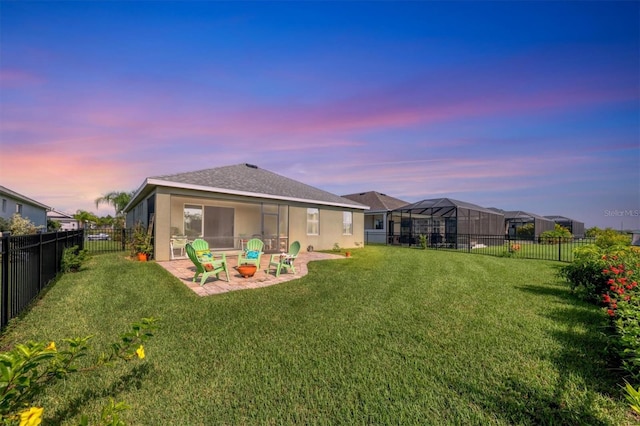 back house at dusk featuring a patio area, a lawn, and glass enclosure