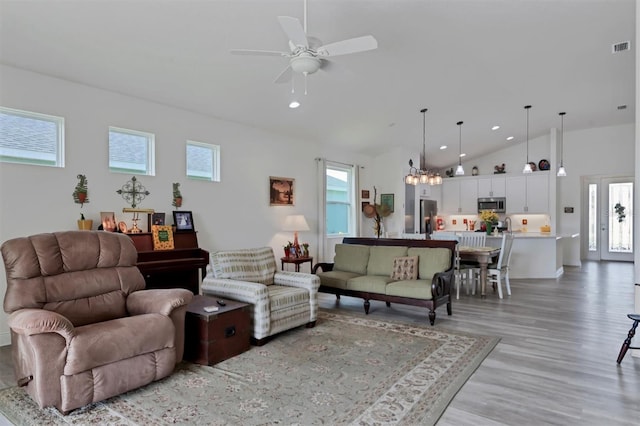 living room with ceiling fan with notable chandelier, light hardwood / wood-style floors, and high vaulted ceiling