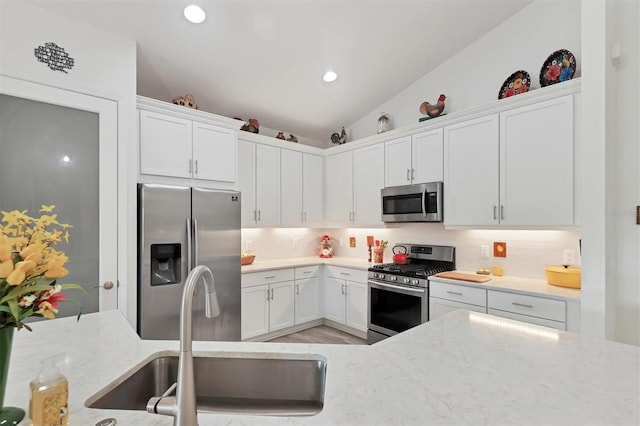 kitchen with stainless steel appliances, white cabinets, sink, lofted ceiling, and backsplash