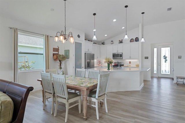 dining space with light hardwood / wood-style floors, high vaulted ceiling, and an inviting chandelier