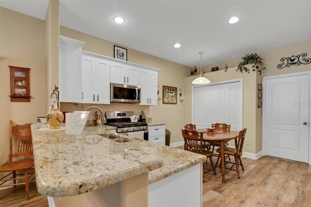 kitchen featuring white cabinetry, appliances with stainless steel finishes, hanging light fixtures, light stone countertops, and light wood-type flooring