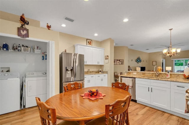 dining space with light wood-type flooring, sink, washer and clothes dryer, and a chandelier