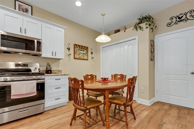 kitchen with light stone counters, appliances with stainless steel finishes, white cabinets, decorative light fixtures, and light wood-type flooring