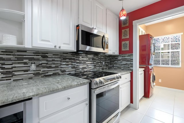 kitchen with appliances with stainless steel finishes, white cabinets, pendant lighting, stacked washer / dryer, and backsplash