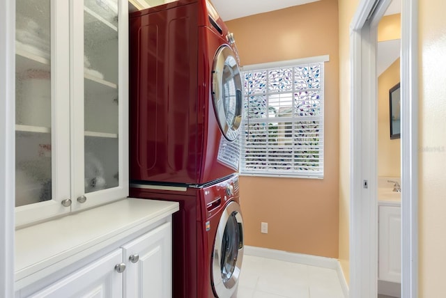 laundry room featuring stacked washer / dryer, cabinets, and light tile patterned flooring