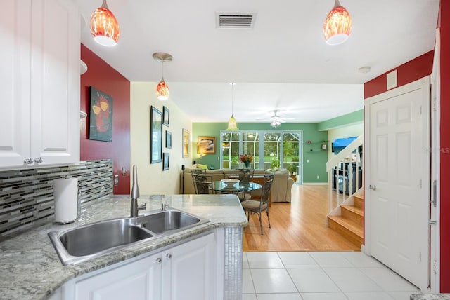 kitchen featuring light tile patterned floors, decorative backsplash, white cabinets, sink, and decorative light fixtures