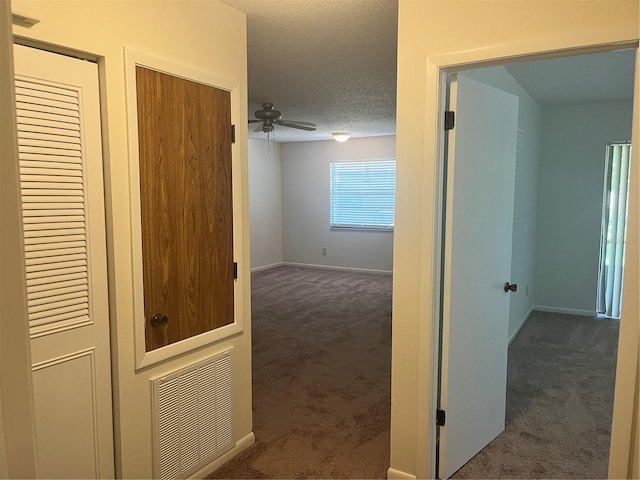 hallway featuring dark carpet and a textured ceiling