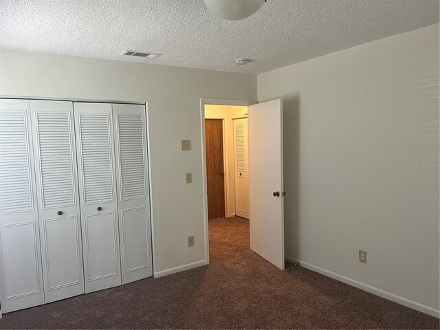 unfurnished bedroom with dark colored carpet, a textured ceiling, and a closet