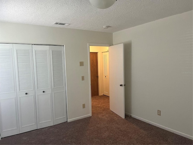 unfurnished bedroom with a textured ceiling, a closet, and dark colored carpet