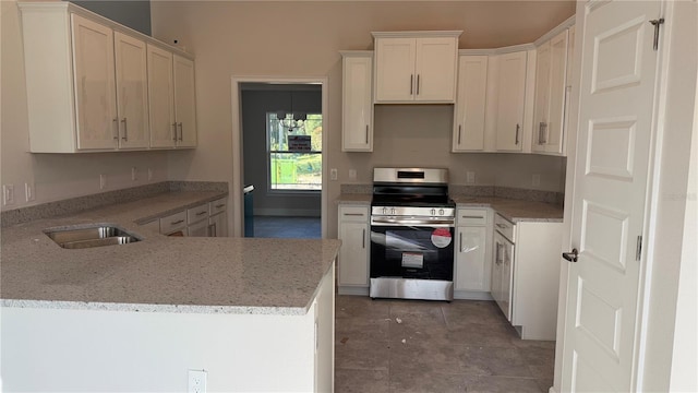 kitchen with light stone countertops, kitchen peninsula, sink, stainless steel stove, and white cabinetry