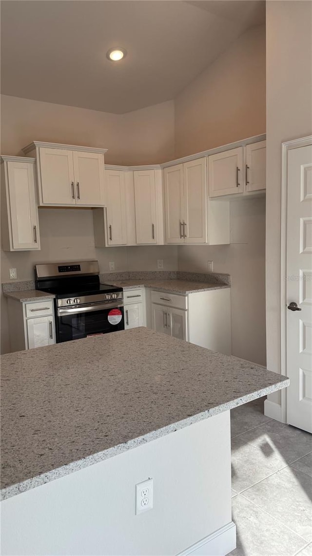 kitchen with high vaulted ceiling, stainless steel stove, light tile patterned flooring, light stone counters, and white cabinetry