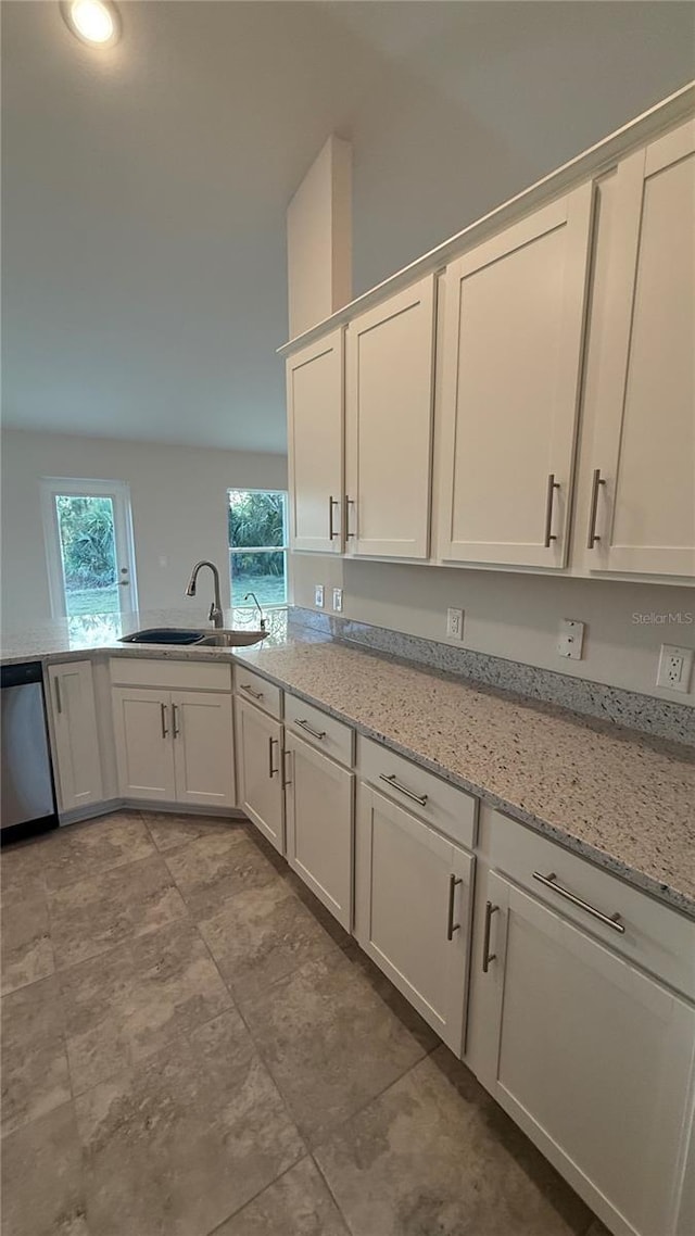 kitchen featuring light stone countertops, white cabinetry, stainless steel dishwasher, and sink