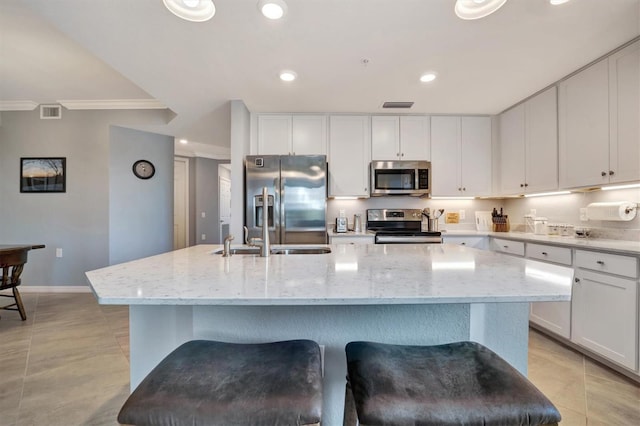 kitchen with white cabinetry, appliances with stainless steel finishes, a kitchen island with sink, and light stone counters