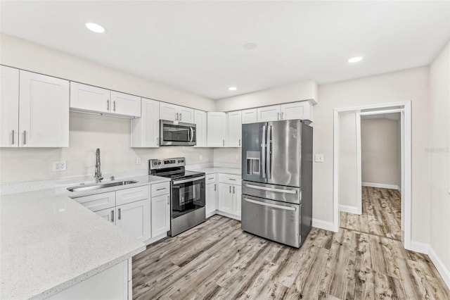 kitchen with stainless steel appliances, white cabinets, sink, light stone counters, and light hardwood / wood-style floors