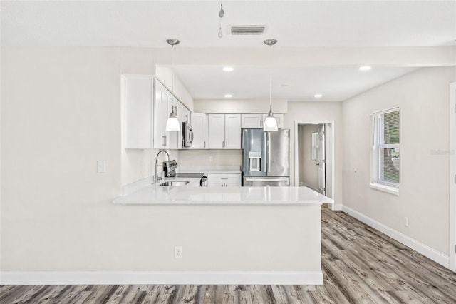 kitchen featuring light hardwood / wood-style flooring, kitchen peninsula, white cabinets, appliances with stainless steel finishes, and pendant lighting