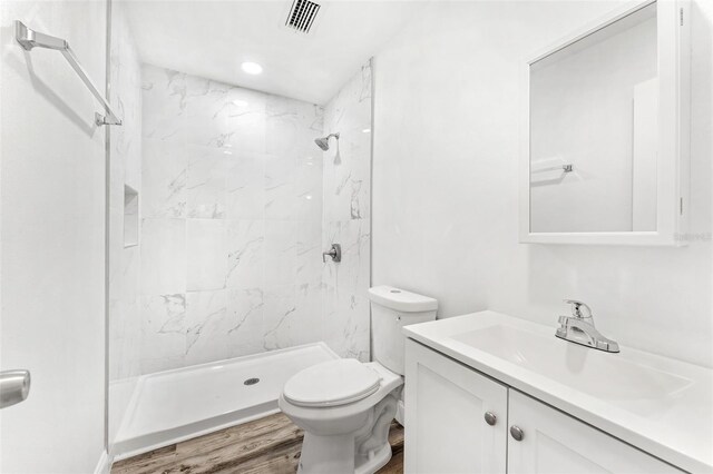 bathroom with a tile shower, vanity, hardwood / wood-style flooring, and toilet