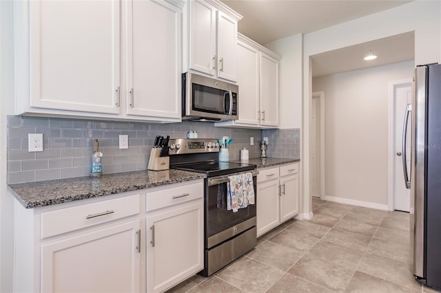 kitchen with white cabinetry, stainless steel appliances, backsplash, and dark stone counters