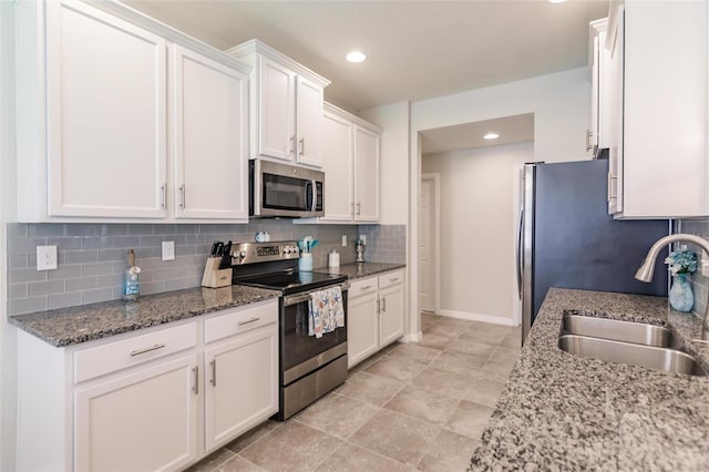 kitchen with white cabinetry, appliances with stainless steel finishes, sink, and dark stone countertops