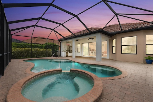 pool at dusk featuring a patio, a lanai, an in ground hot tub, and ceiling fan