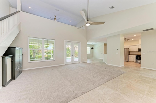 unfurnished living room featuring ceiling fan, french doors, light colored carpet, and a towering ceiling