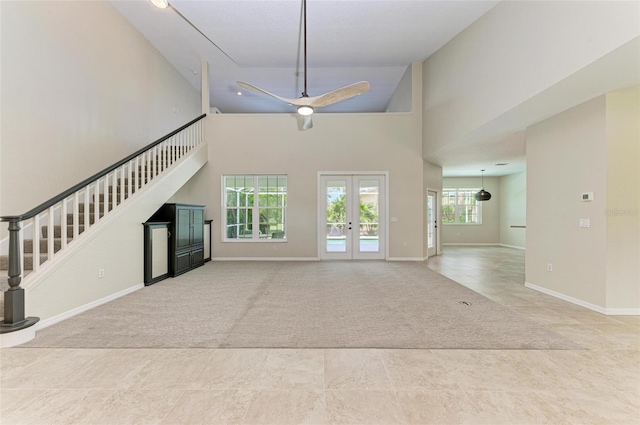 unfurnished living room featuring light carpet, french doors, ceiling fan, and a high ceiling