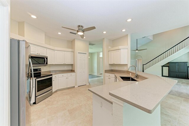 kitchen featuring kitchen peninsula, appliances with stainless steel finishes, white cabinets, and ceiling fan